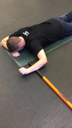 a man laying on the ground with an orange baseball bat in his hand and wearing black shirt