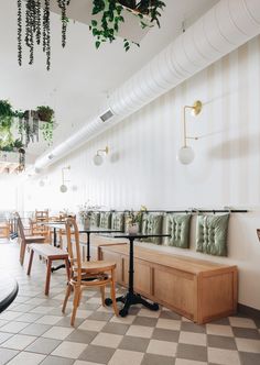 an empty restaurant with wooden chairs and green plants hanging from the ceiling, along with checkered tile flooring