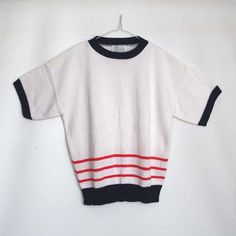 This is a sweet, knitted nautical top with anchors and stripes. It has a big knit anchor at the front and a smaller version on each of the sleeves, three red stripes run along the bottom and all of the edges are finished with a navy yarn.It is of a MEDIUM size. For label details, please see images.The measurements (when laid flat) are as follows.Bust: 53cmWaist: 50cmHemline: 37cmLength: 57cmSleeve Length: 15cmIt is in an excellent condition!Perfect with jeans and shorts for chilly summer evening Knit Tops With Striped Sleeves And Crew Neck, Knit Crew Neck Tops With Striped Sleeves, White Crew Neck Sweater With Striped Sleeves, White Nautical Crew Neck Top, White Knit Sweater With Contrast Stripes, White Casual Tops With Sailor Collar, Casual White Sailor Collar Top, Nautical Vintage, Big Knits