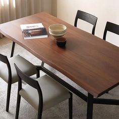 a wooden table with four chairs and a bowl on it in front of a window