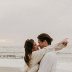 a man and woman holding each other on the beach