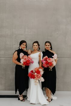 three bridesmaids in black and white dresses with red bouquets standing next to each other