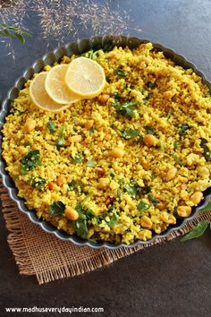 a dish filled with rice and vegetables on top of a table next to lemon wedges