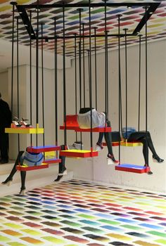 two people are sitting on swings suspended from the ceiling in an art installation with multicolored flooring