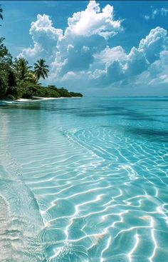 the water is very clear and blue with some clouds in the sky above it on an island