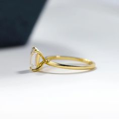 a yellow gold ring with an oval cut diamond on the side, sitting on a white surface