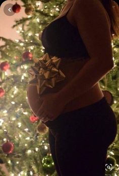 a pregnant woman standing in front of a christmas tree with her belly wrapped around the waist