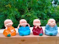 four small buddha figurines sitting on top of a wooden table next to trees