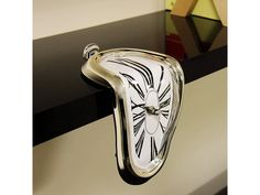 a glass clock hanging from the side of a wall in front of a black and white striped wall