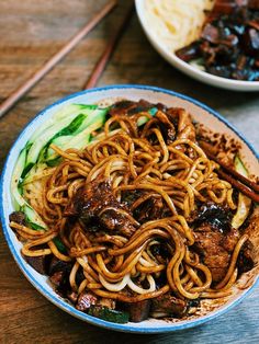 a bowl filled with noodles and meat on top of a wooden table next to chopsticks