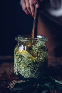 a jar filled with pickles on top of a wooden table next to green leaves