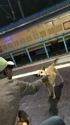 a man is petting a small dog on the train platform while another person looks on