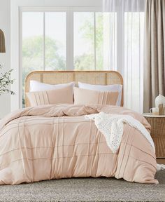 a bed with pink comforter and pillows in a room next to a window,