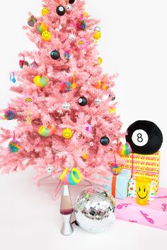 a pink christmas tree decorated with embellishments and smiley face ornaments next to a disco ball