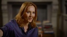 a woman with red hair and blue shirt giving the thumbs up in front of her