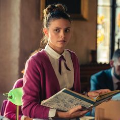 a woman holding a book in her hands while sitting at a table with other people