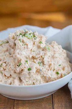 a white bowl filled with chicken salad sitting on top of a wooden table next to a napkin