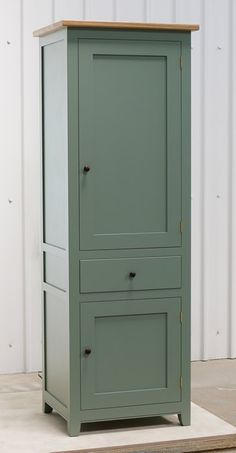 a tall green cabinet sitting on top of a wooden floor next to a white wall