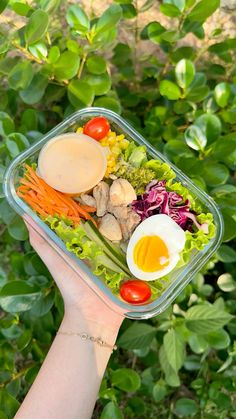 a person holding up a plastic container filled with vegetables and an egg on top of it