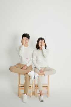 two people sitting on chairs with their hands to their faces