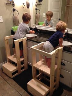 two young boys are playing in the bathroom mirror with their own wooden step stools