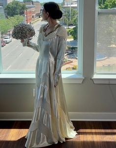 a woman standing in front of a window with a bouquet of flowers on her hand