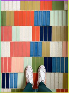 a person's feet in white sneakers standing on a multicolored tile floor