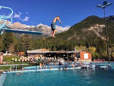 a man jumping into a swimming pool with mountains in the background