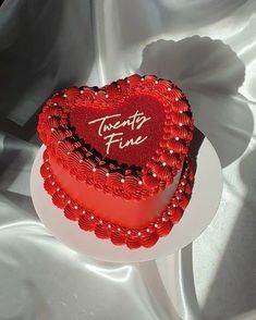 a red heart shaped cake sitting on top of a white platter next to a silver cloth