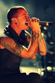 a man singing into a microphone with tattoos on his arm and chest, in front of the words i wanna't be used aside so let me go