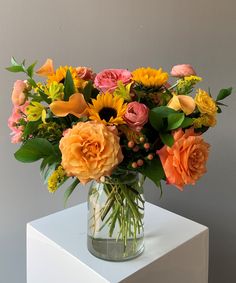 a vase filled with lots of different colored flowers on top of a white table next to a gray wall