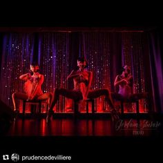 three women are sitting on chairs in front of a stage with purple and red lights