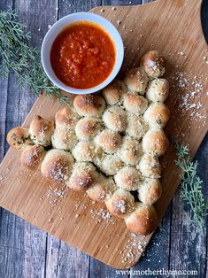 a wooden cutting board topped with rolls covered in cheese and tomato sauce next to a bowl of dipping sauce