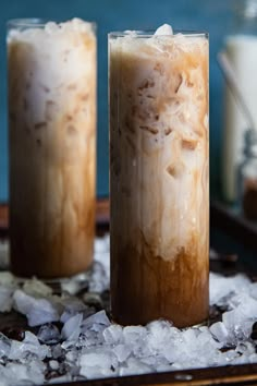 two tall glasses filled with iced coffee on top of ice covered ground next to bottles