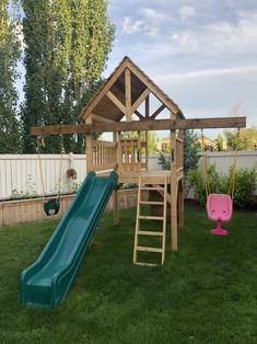 a wooden playset with a slide and swing set in the back yard, next to a white picket fence