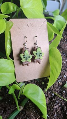 a pair of green and brown earrings sitting on top of a leafy plant next to a