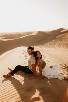 a man and woman sitting on top of a sandy beach next to each other in the desert