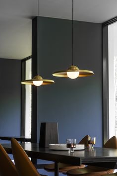 a dining room table with chairs and lights hanging from it's ceiling, in front of a large window