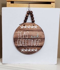 a wooden sign that says seas and greetings hanging on a white board with wood beads