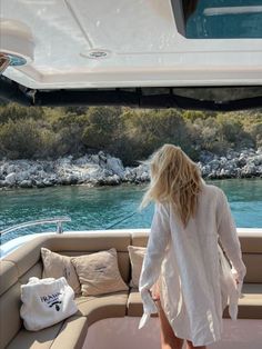 a woman is standing on the back of a boat looking out at the water and rocks