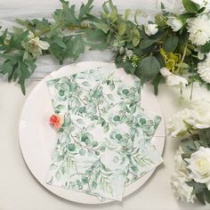 a plate with napkins and flowers on it sitting next to some green leaves in the background