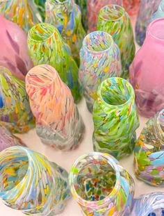 many different colored vases sitting on top of a white tablecloth covered floor with colorful paint splatters all over them