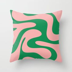 a pink and green pillow with an abstract design on the front, sitting against a white wall