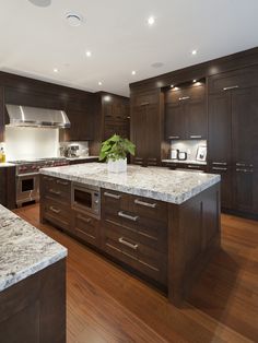 a large kitchen with marble counter tops and dark wood cabinets, along with stainless steel appliances