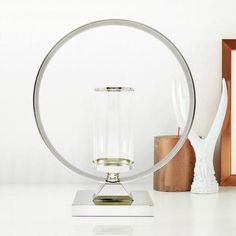 a white table topped with a glass and metal object next to a wooden frame on top of a desk