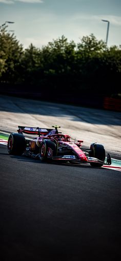 a red racing car driving on a race track with trees in the background at dusk