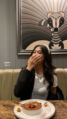 a woman covering her mouth while sitting at a table with a chocolate cake on it