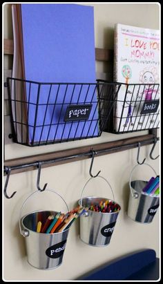 two metal buckets with pencils and markers are hanging on the wall next to books