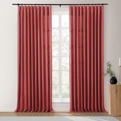 a red curtain hanging in front of a window with white walls and wooden flooring