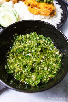 a black bowl filled with green sauce next to rice and cucumber wedges